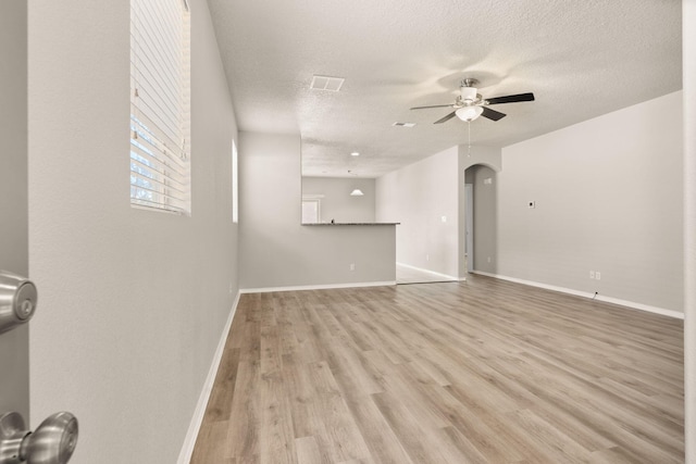 unfurnished living room with a textured ceiling, arched walkways, light wood finished floors, baseboards, and ceiling fan