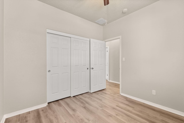 unfurnished bedroom with a textured ceiling, a closet, light wood-style floors, baseboards, and ceiling fan