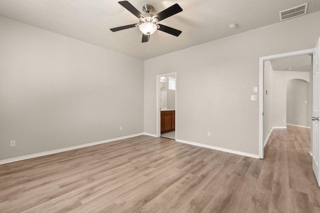 unfurnished bedroom with visible vents, baseboards, light wood-style flooring, arched walkways, and a textured ceiling