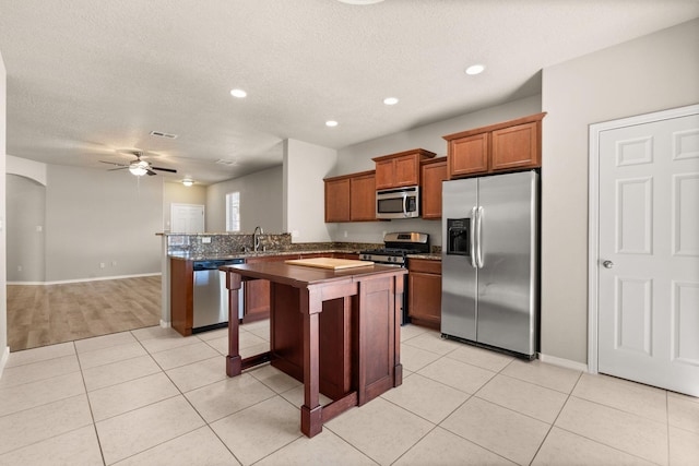 kitchen with brown cabinets, dark countertops, appliances with stainless steel finishes, light tile patterned flooring, and ceiling fan