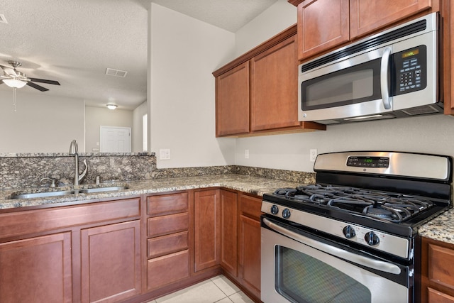 kitchen featuring stainless steel appliances, stone countertops, a textured ceiling, a ceiling fan, and a sink