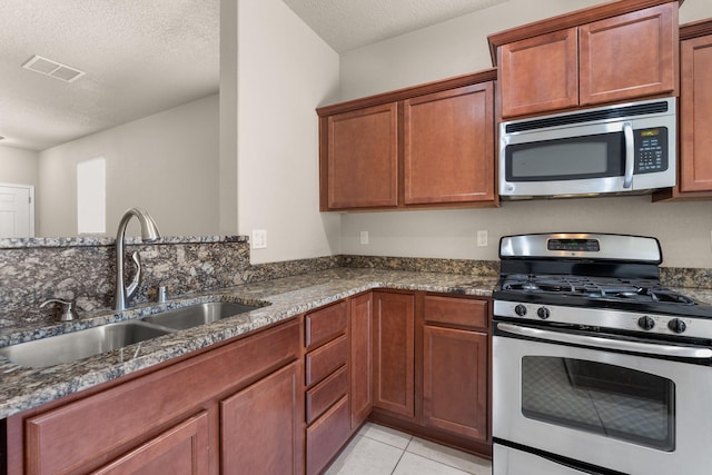 kitchen featuring visible vents, dark stone countertops, stainless steel appliances, a textured ceiling, and a sink