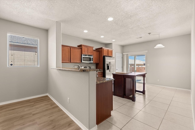 kitchen with a peninsula, baseboards, brown cabinets, and appliances with stainless steel finishes