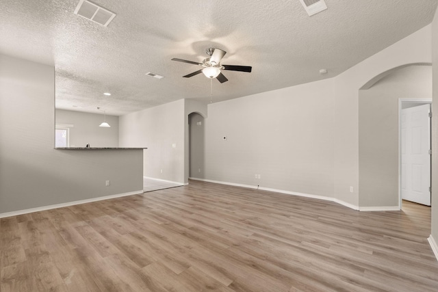 empty room with light wood-style floors, visible vents, a ceiling fan, and arched walkways