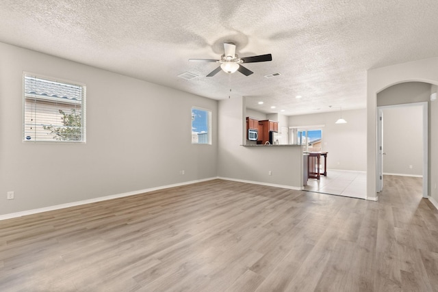 unfurnished living room featuring visible vents, arched walkways, a ceiling fan, and light wood finished floors