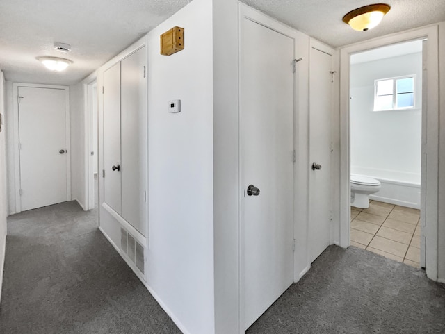 hall with tile patterned flooring, carpet, and a textured ceiling