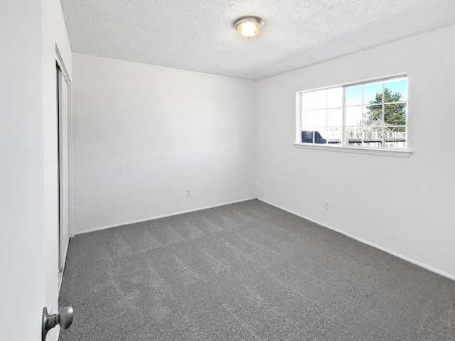 unfurnished bedroom with a closet, a textured ceiling, baseboards, and dark colored carpet