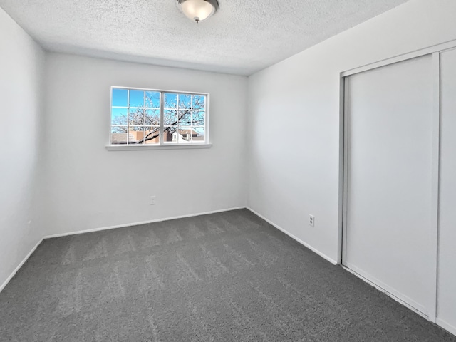 unfurnished room with baseboards, a textured ceiling, and dark carpet