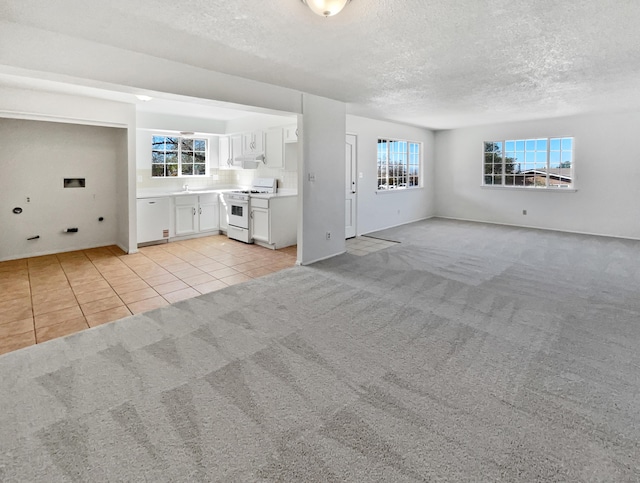 unfurnished living room featuring light tile patterned flooring, light colored carpet, and a textured ceiling