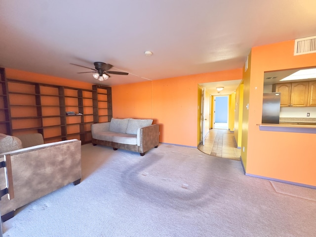 living area with visible vents, light colored carpet, baseboards, and ceiling fan