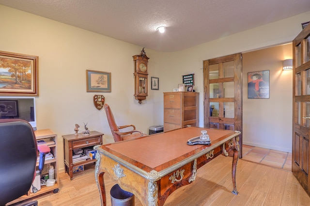 office area featuring light wood-type flooring, baseboards, and a textured ceiling