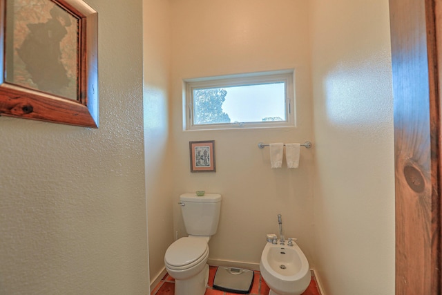 bathroom with toilet, a bidet, and baseboards