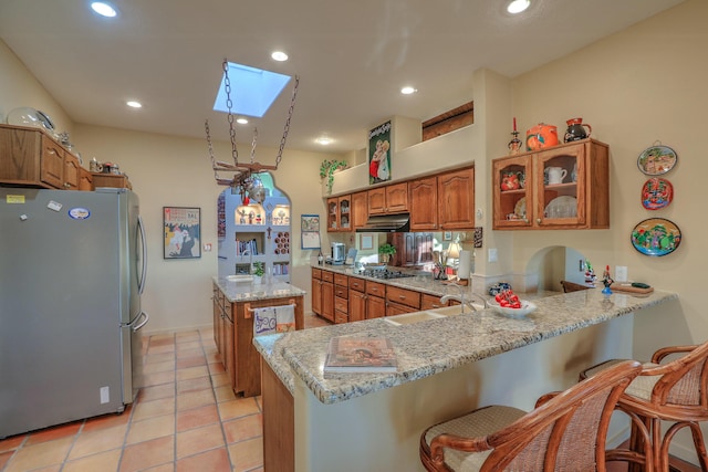 kitchen with brown cabinetry, a skylight, a sink, under cabinet range hood, and appliances with stainless steel finishes