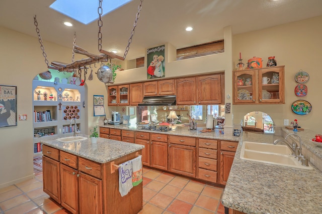 kitchen with gas cooktop, brown cabinets, under cabinet range hood, and a sink