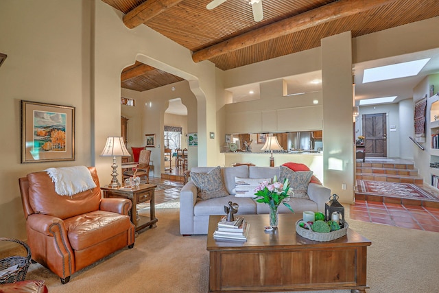 living area with carpet, beam ceiling, a skylight, a towering ceiling, and wooden ceiling