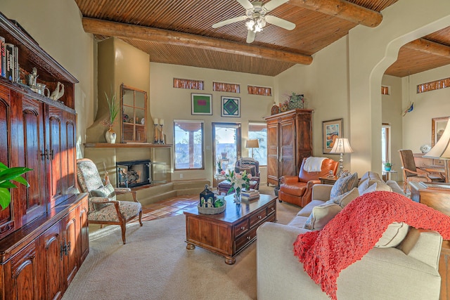 living area with beamed ceiling, a fireplace with raised hearth, arched walkways, wooden ceiling, and ceiling fan