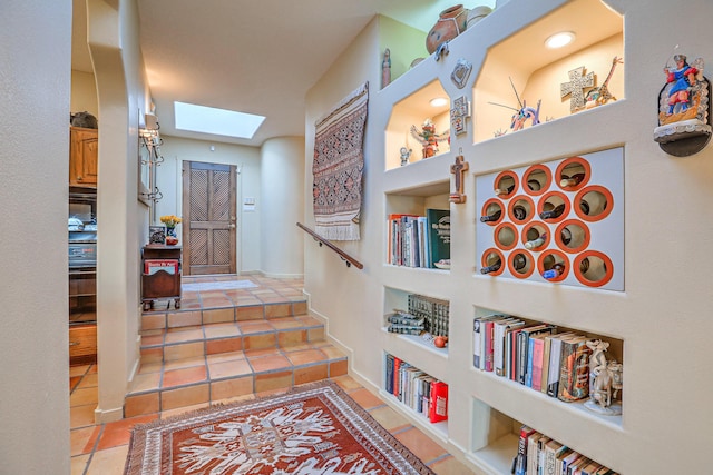 hallway with light tile patterned floors, built in features, and a skylight