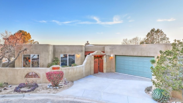 adobe home with a garage, fence, concrete driveway, and stucco siding