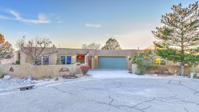 pueblo-style home with a fenced front yard, a garage, driveway, and stucco siding