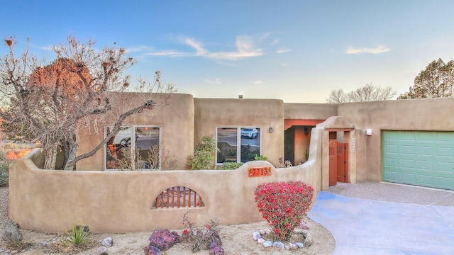 pueblo-style home with a fenced front yard, an attached garage, and concrete driveway