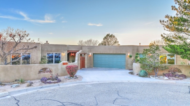 pueblo revival-style home featuring stucco siding, concrete driveway, and a garage