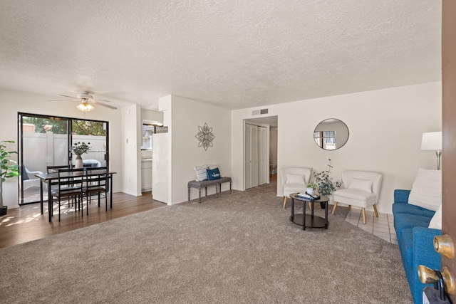 living area featuring carpet flooring, visible vents, a textured ceiling, and a ceiling fan