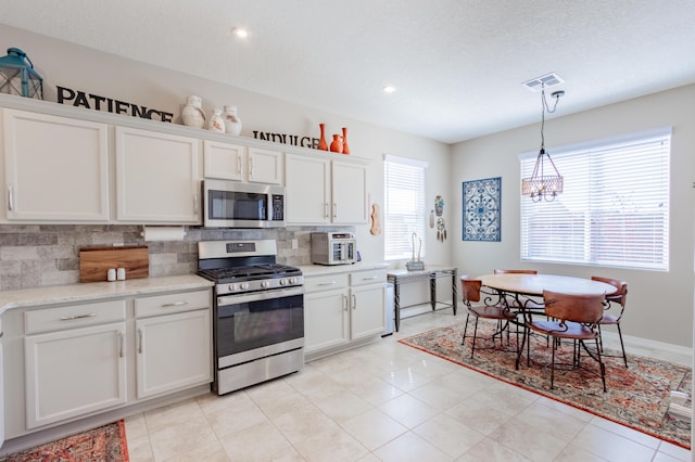 kitchen featuring visible vents, stainless steel appliances, decorative backsplash, white cabinets, and a chandelier