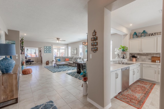 kitchen with open floor plan, dishwasher, light countertops, white cabinetry, and a sink