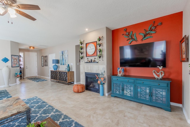 living area featuring a textured ceiling, a fireplace, baseboards, and ceiling fan