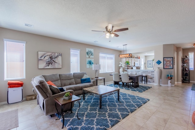 living area with visible vents, baseboards, ceiling fan, light tile patterned floors, and a textured ceiling