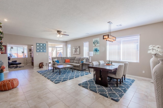 dining space with light tile patterned floors, a ceiling fan, baseboards, visible vents, and a textured ceiling