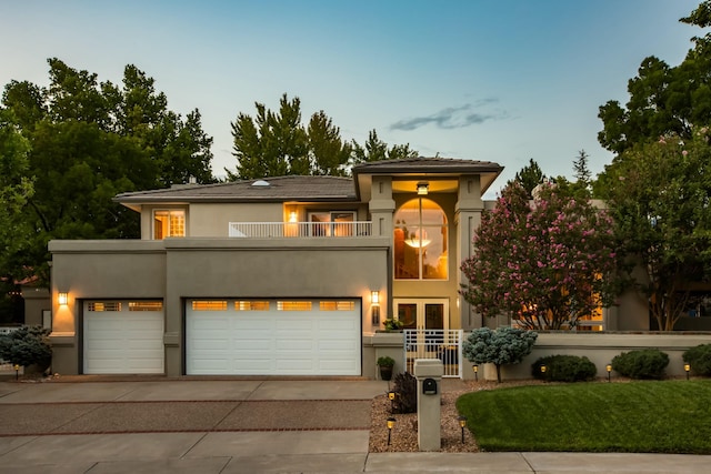 view of front facade featuring french doors, a balcony, concrete driveway, and stucco siding