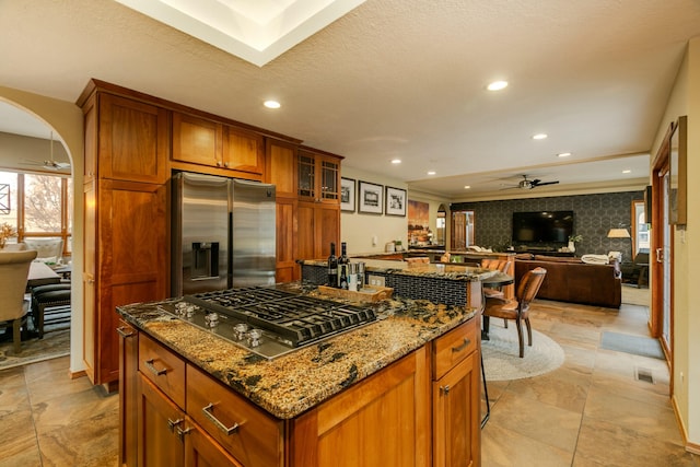 kitchen featuring a center island, stainless steel appliances, brown cabinetry, wallpapered walls, and ceiling fan