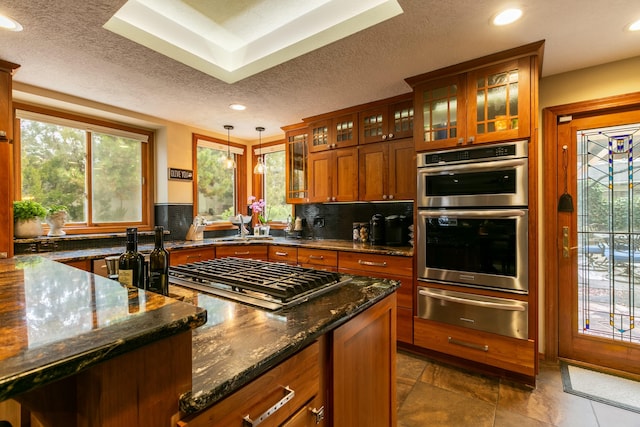 kitchen featuring a warming drawer, dark stone countertops, backsplash, stainless steel appliances, and brown cabinetry