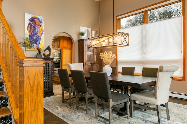 dining space featuring arched walkways, stairway, a high ceiling, and wood finished floors