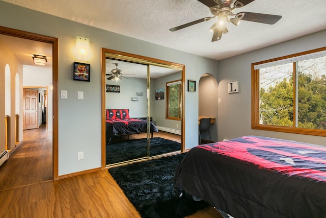 bedroom featuring a textured ceiling, wood finished floors, a closet, arched walkways, and a baseboard radiator