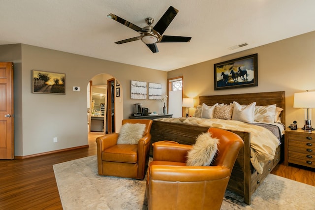 bedroom featuring wood finished floors, arched walkways, visible vents, and baseboards