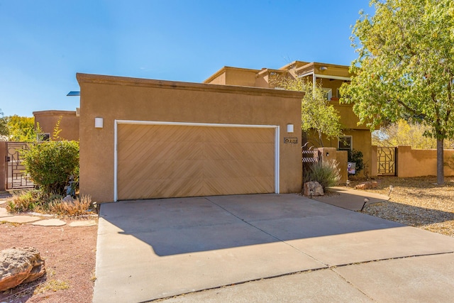 pueblo-style house featuring concrete driveway, a gate, and stucco siding