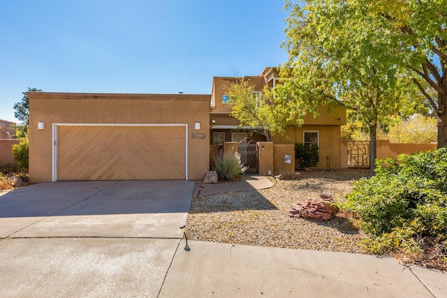 pueblo-style home with stucco siding, driveway, a garage, and a gate