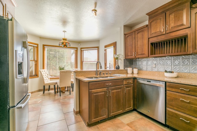 kitchen featuring a sink, tasteful backsplash, stainless steel appliances, a peninsula, and brown cabinetry