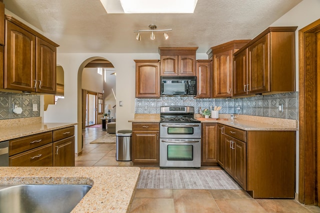 kitchen with arched walkways, decorative backsplash, appliances with stainless steel finishes, and a sink