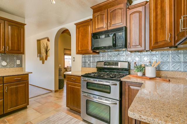 kitchen featuring brown cabinetry, double oven range, arched walkways, black microwave, and backsplash