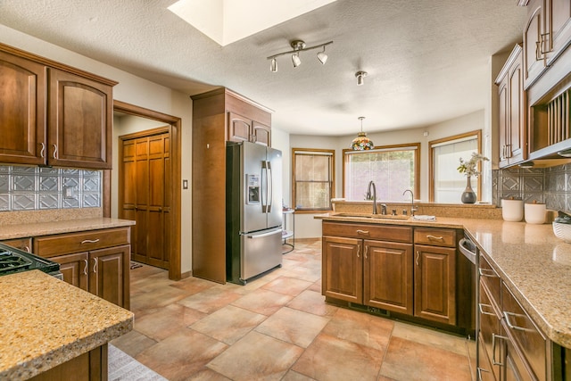 kitchen featuring a sink, appliances with stainless steel finishes, a peninsula, a skylight, and decorative backsplash