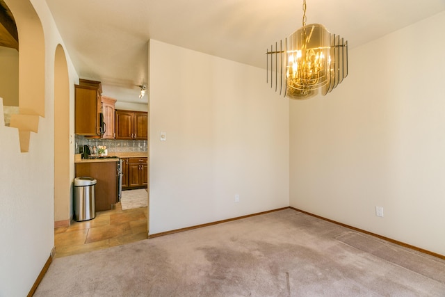 unfurnished dining area featuring arched walkways, light colored carpet, baseboards, and an inviting chandelier