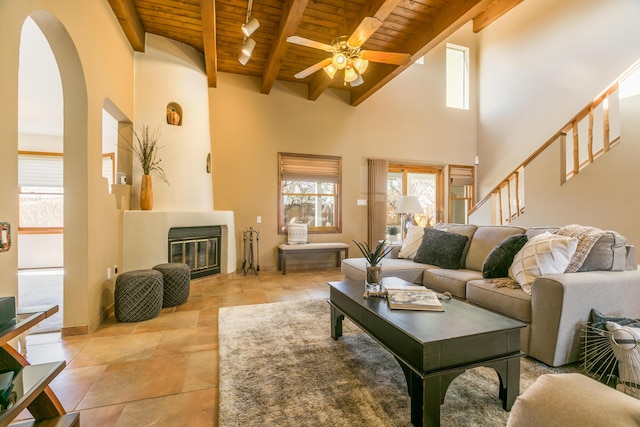 living room featuring stairway, ceiling fan, wood ceiling, beamed ceiling, and a large fireplace