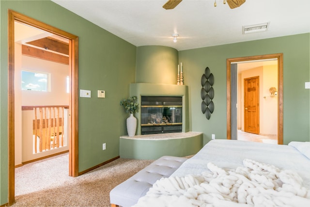 bedroom with visible vents, a ceiling fan, a glass covered fireplace, carpet, and baseboards