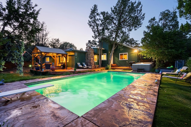 pool at dusk with a wooden deck, an outdoor pool, and a hot tub