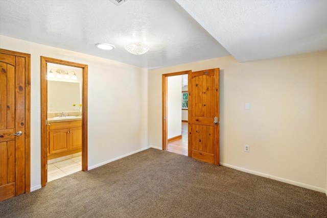 unfurnished bedroom with a textured ceiling, a sink, baseboards, and light carpet