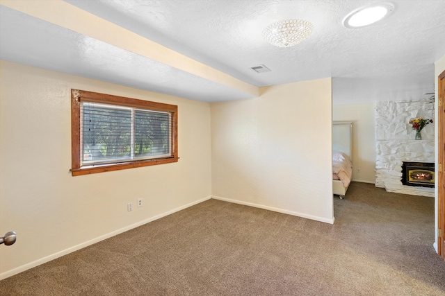 carpeted empty room featuring visible vents, a fireplace, a textured ceiling, and baseboards