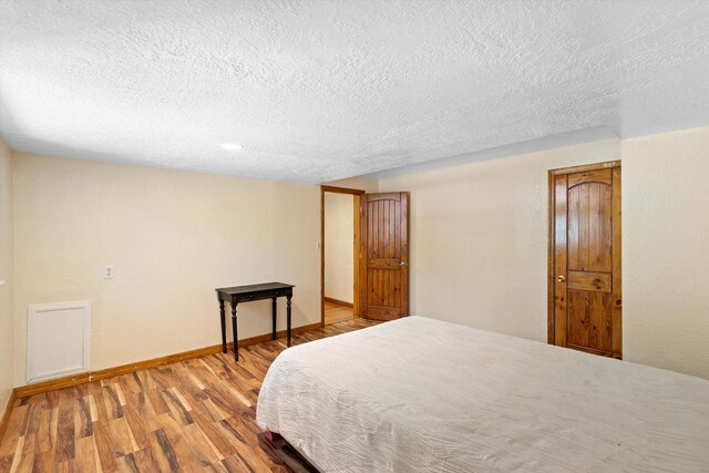 bedroom featuring light wood-type flooring, baseboards, and a textured ceiling